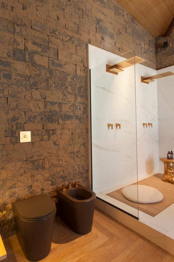 A parede ganhou a textura suave do revestimento Ecobrick Stone Cappuccino e combinou com o uso de metais dourados no banheiro.
